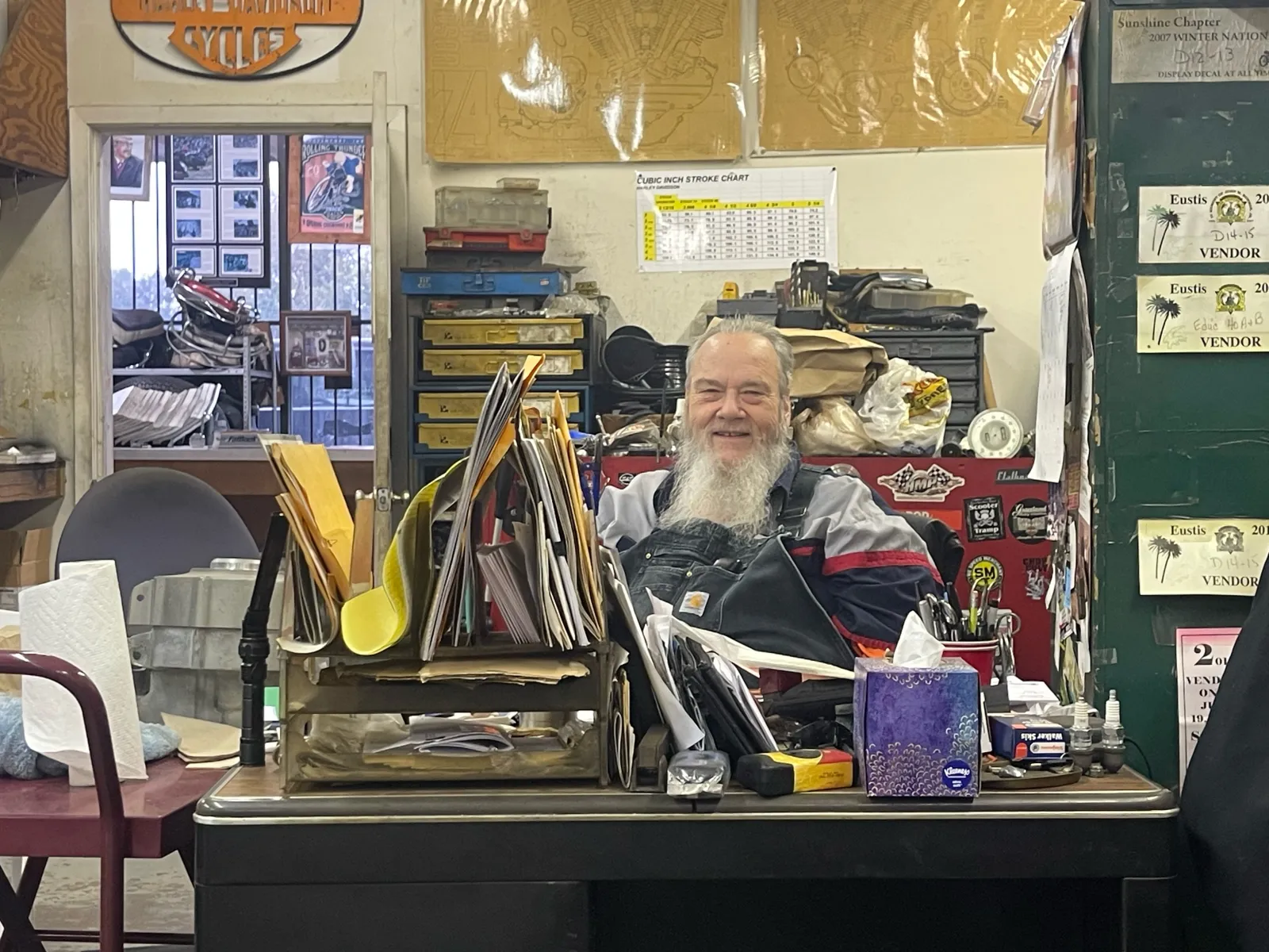 Greg Hale at the McCreations counter — bearded, smiling, papers and vendor displays on the desk